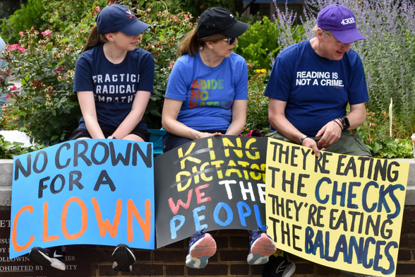Three people with signs at a No Kings rally in Alexandria, Va. 14 June 2025