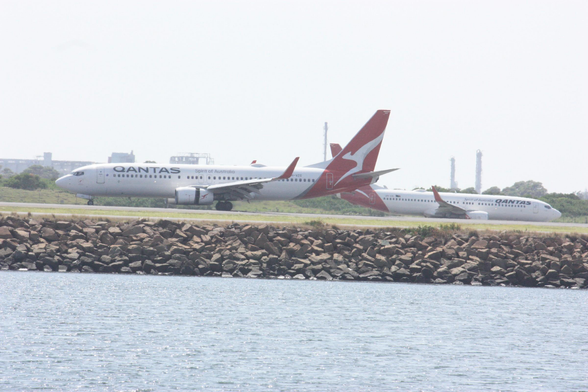 two Qantas Boeing 737-800NGs at Sydney Airport, one in front of the other in this perspective. The nearer one, reg VH-VZG, is landing and has thrust reversers deployed. The far one, reg VH-VXL, is on a taxiway.
photo by Ian Kluft
27 January 2025
Sydney Kingsford Smith Airport SYD/YSSY, Sydney, New South Wales, Australia
