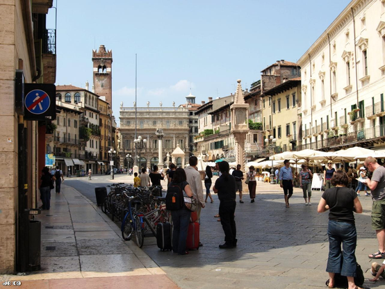 Farbfoto, aufgenommen auf der Piazza delle Erbe in Verona, Veneto, Italien. Der große Platz ist umgeben von historischen Gebäude und bevölkert von zahlreichen Passanten.