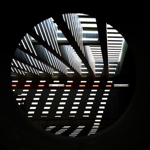 Sunlight shining to a grid, projecting abstract patterns to the insides of a tunnel. Seen through a round hole in a wall.