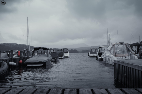 Monochrome shot of small boats at wooden jetty on lake water 