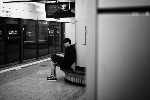 A person sits in the subway platform seat looking at a laptop
