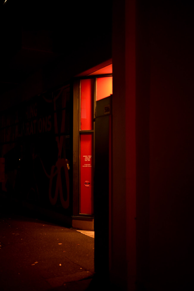 A red glow emerges from an obscured shop door onto the footpath