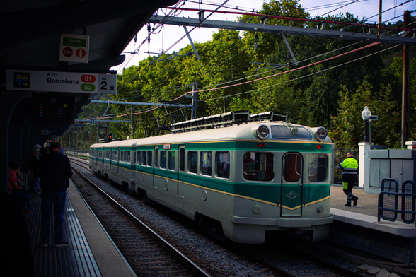 The "frog" train parked at the siding of Les Planes station. On the front of the train, there's the logo of Ferrocarrils de Catalunya, which built the train and used to operate this line. There are signs on the side of the train indicating "Tarrasa" in capital letters.