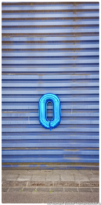 A lonely blue inflated birthday ballon in a "0" shape hangs on the front of a blue building.