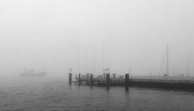 Schwarz-Weiß Ansicht des Anlegers Reventlou. Im Nebel fährt ein Forschungsschiff des Geomar