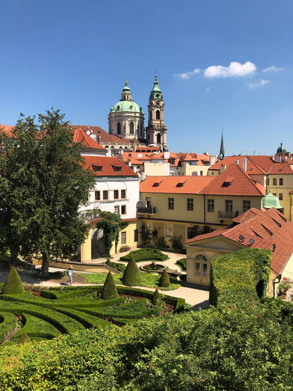 The manicured gardens and buildings of Vrtba gardens in Prague. The sky is a bright blue with one cloud visible 