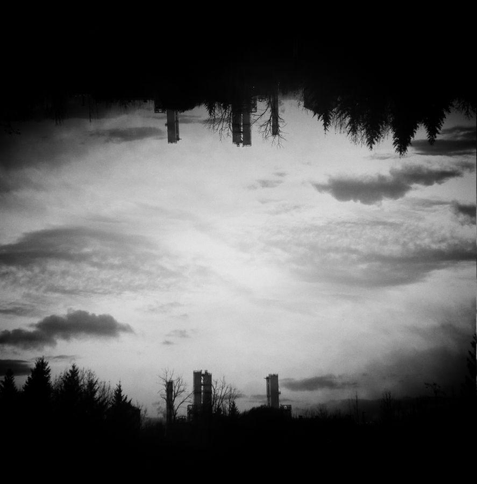 Black and white skyline with trees and industrial buildings. There are detailed clouds that form a dynamic diagonal line through the composition.