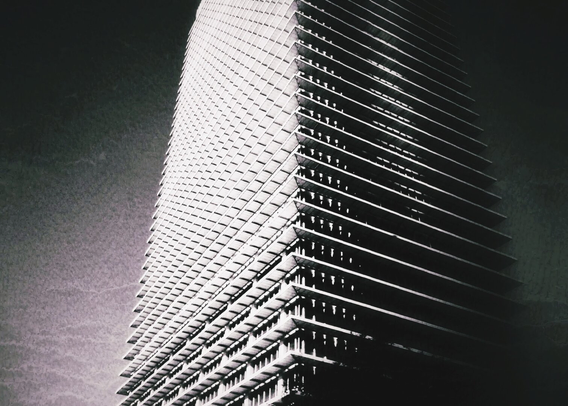 A black and white photo showing a low angle view of a tall apartment tower.