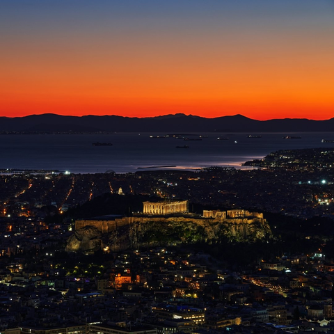 Sunset over the city of Athens. The sky glows orange with the lights of the city turns on below. I'm the centre of the photograph, rising above the rest of the city, is the Acropolis and the Parthenon.