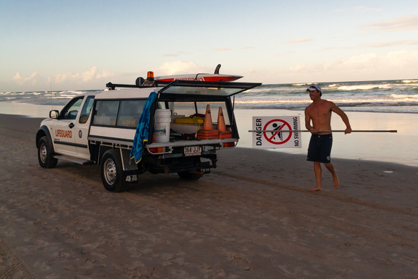 A surf lifesaver putting a danger, no swimming sign away into the back of a vehicle on a beach.
