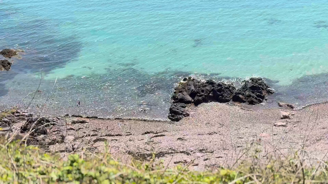 Video of a few gentle waves shimmering under the sun around some rocks on a beach 