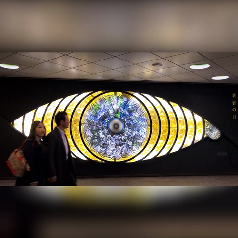 Gente (mayoritariamente empleados de las oficinas del centro) pasando por delante de un gran ojo de cristal iluminado, de unos 4 metros de ancho, diría yo.