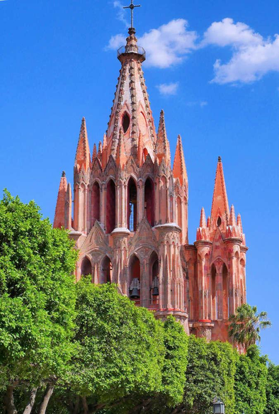 Top spires of La Parroquia de San Miguel Arcángel in San Miguel de Allende, Mexico, with green trees in the foreground