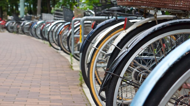 The rear wheels of numerous bicycles follow the curve of a sidewalk.