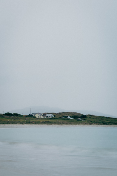 an ocean shore with houses on a grassy hill