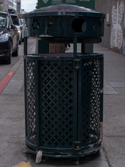Image of a steel-green metal trash can on the sidewalk a San Francisco street.