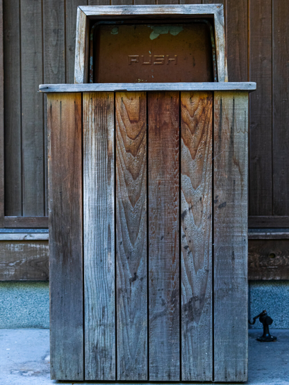 Image of an aged, wooden trash bin. The opening for garbage is a worn metal door with the word "Push" printed on it.