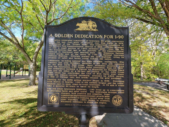 Photo of a sign along a bike trail, titled "A Golden Dedication For I-90" along with several paragraphs of historical information.