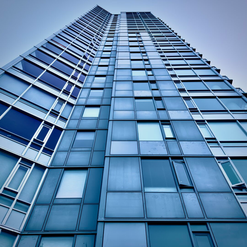 A upward perspective of Benson Tower apartment building reveals a vivid blue reflection of the morning sky above against a metal and glass exterior.