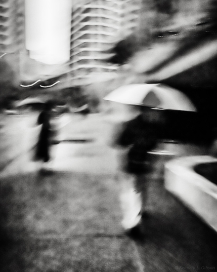 ICM image of people with umbrellas in urban area.