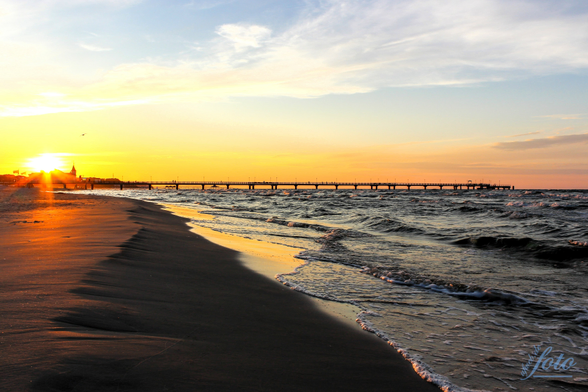 Das Foto ist klassisch und wirkungsvoll zugleich. Die Seebrücke Ahlbeck's führt das Auge direkt in das Herz des Sonnenuntergangs, der als zentraler Punkt wirkt. Der dunkel wirkende Sandstrand im Vordergrund erzeugt eine räumliche Tiefe und betont die Weite des Himmels. Die sanften Wellen zeichnen eine klare Linie zwischen Land und Meer. Der stilistische Ansatz ist eher realistisch, aber durch die warme Farbgebung und den Fokus auf den Sonnenuntergang entsteht eine romantische und friedliche Stimmung.

Heute mal ein KI- generierter Text, da mir irgendwie die Worte fehlen.