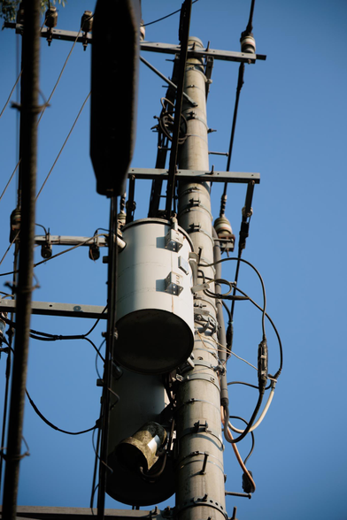 Close-up of a utility pole with power lines and a transformer against a blue sky.