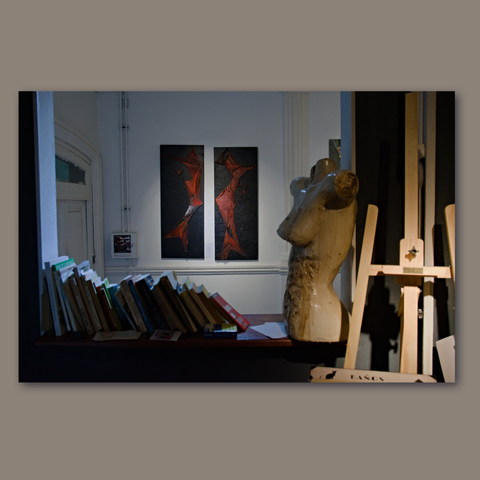 Two paintings behind an internal window with some books and a mannequin.