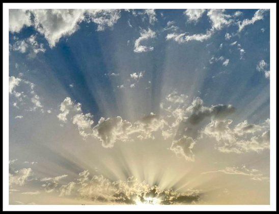 Blue and yellow sky filled with clouds and rays of sunlight radiating from the horizon, creating a captivating and serene atmosphere.