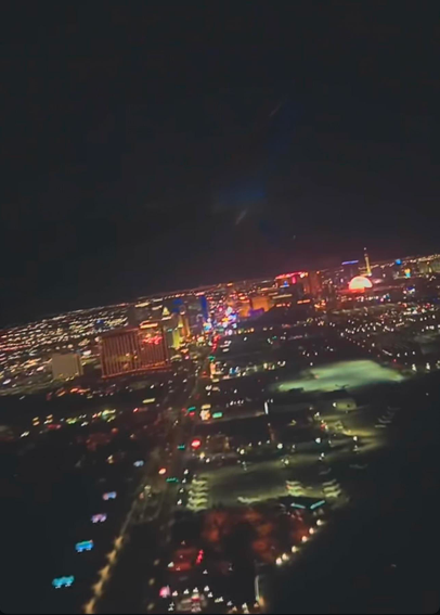 This is a night time photo taken from a window inside a commercial passenger airplane as it takes off toward the southwest from the Harry Reid Airport (formerly the McCarran Airport). In the distance, the iconic Sphere is seen fully lit to resemble a full moon. More in the foreground is a lit up golf course and the street lights leading toward the Strip and multiple hotel/casinos with multi-colored lights that appear mostly red and yellow against a dark night sky. The photo was taken with an Apple iPhone 16 pro plus.