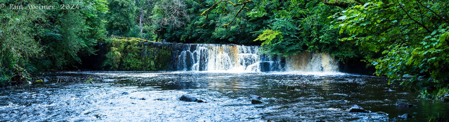 Wide knitted shots of a short but wide waterfall with greenery 