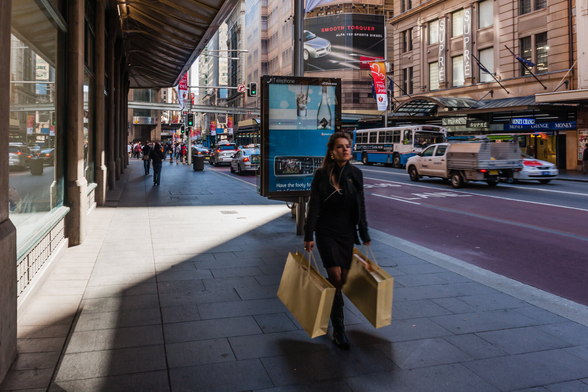 A woman with two large shopping bags walks along Sydney's main Street, George Street.