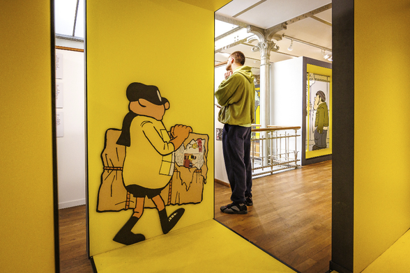 A man is observing something not visible for the viewer in a Museum between two yellow panels with human size comics character. The character on the left represents a thief sneaking away with a painting. He seems to be saising the occasion that the visitor is looking in another direction to pass by behind him. The second character is wearing clothes of the same colour as the museum visitor.
