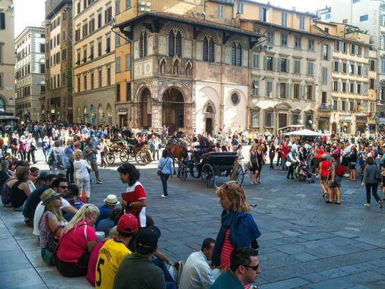 A crowded and hectic scene in the Piazza del Duomo, Florence. The steps are packed with seated, weary tourists and the square is thronged with horse-carriages, street vendors, performers and everywhere tourists. It's a sunny day, but obviously not hot.