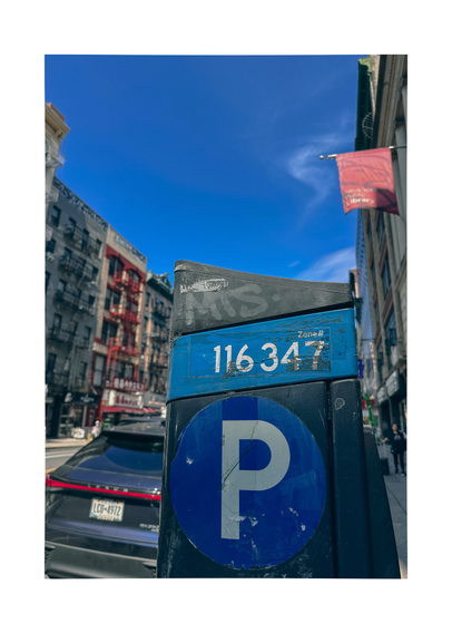 A parking meter kiosk with a white P in a blue circle on a city street. Above is a blue sky