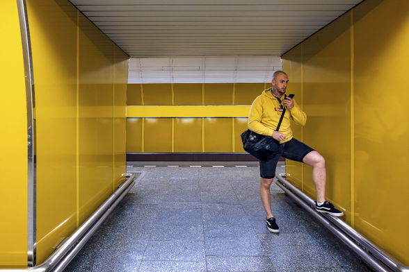 A man with a yellow sweater is waiting on a metro platform in a yellow alcove in a Prague metro station.