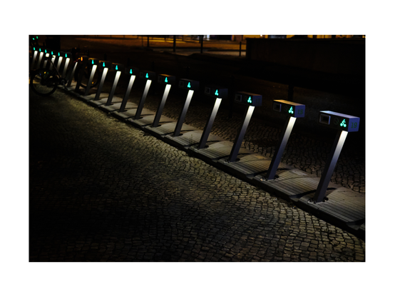 bicycle parking spaces neatly in a row, lit white and green by night in a lisbon neighborhood