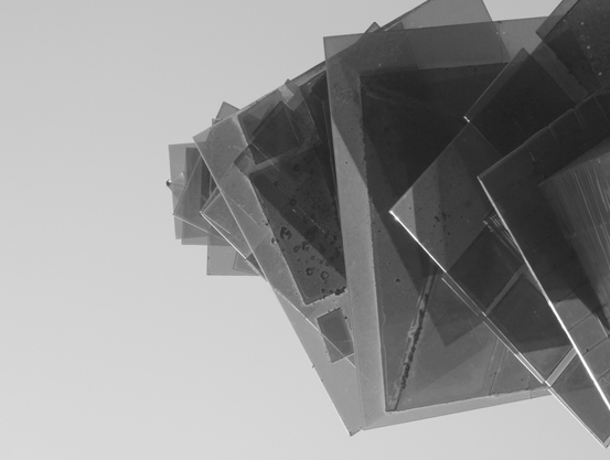 Black and white photography of one of the “glass trees” from below, consisting of various tinted glass squares stacked on top of each other, creating different shades of gray. The lowest and largest is on the right and it gets progressively smaller towards the left until it reaches the top at about a third of the horizontal line 

Schwarz-Weiß-Fotografie eines der „Glasbäume“ von unten, die aus verschiedenen übereinander gestapelten, getönten Glasquadraten bestehen, was verschiedene Grauschattierungen erzeugt.
Das unterste und größte ist rechts und es wird nach links zunehmend kleiner bis zur Spitze bei ca. einem Drittel der Horizontale