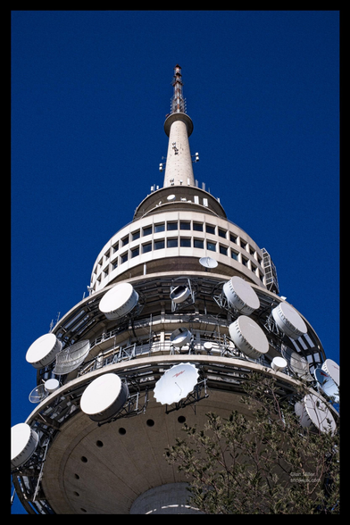 A close-up view of a telecommunications tower with multiple satellite dishes and antennas against a clear blue sky.