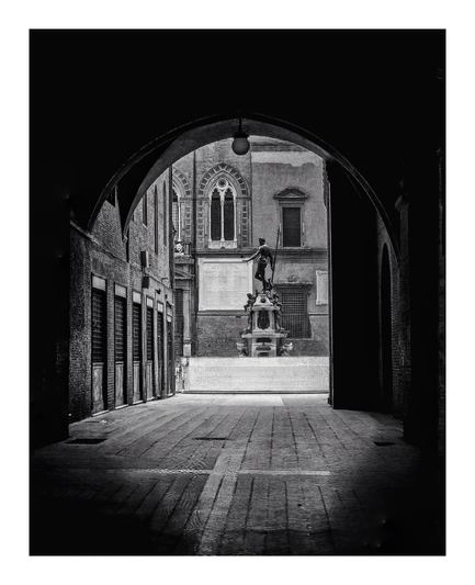 This is a black-and-white photograph showing a dark arched passageway leading outside to a square (Piazza del Nettuno). At the center of the photo, framed by the arch, is a classical statue of a man holding a spear, mounted on an ornate pedestal. The surrounding architecture is largely medieval, with arched windows, brick walls, and a cobbled/tiled floors. There is a strong contrast between the dark and shadowy archway and the brightly lit square outside.