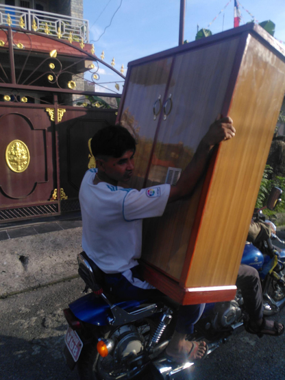 Image of a motorcycle from the side, where the person sitting in the back seat carries a wardrobe