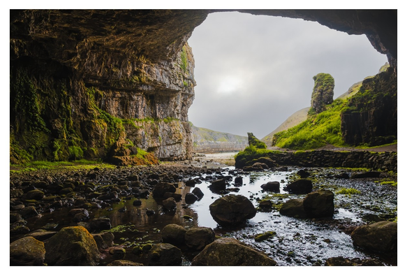Eine beeindruckende Höhle mit üppigem Grün, die den Blick auf einen ruhigen Wasserlauf und sanfte Hügel freigibt, umhüllt von mystischem Nebel.