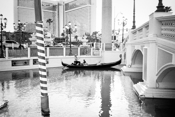 A black and white photograph of a gondola in a river in the middle of a city in the middle of a desert.