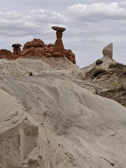 A slope of white rock with wavy patterns leads the eye upwards to a pile of red rocks, some of which are shaped like toadstools.