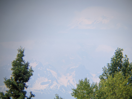 Barely visible snow covered peaks and valleys. Lower peaks fairly defined and upper peaks much higher barely breaking through a mist appearing to be surrounded by a halo of light.