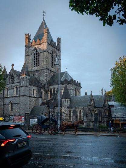 A horse drawn carriage walks the street in front of an old gothic style church.