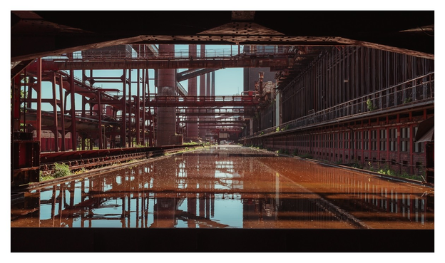 Ein verlassener Industriekomplex spiegelt sich in stillen Wasserflächen, umgeben von rostigen Strukturen und einem Hauch von Natur.