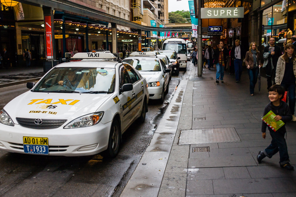 In Pitt Street, in the centre of Sydney, aline of taxis is at the curbside, and on the right a little smiling boy is about to walk out of the scene.
