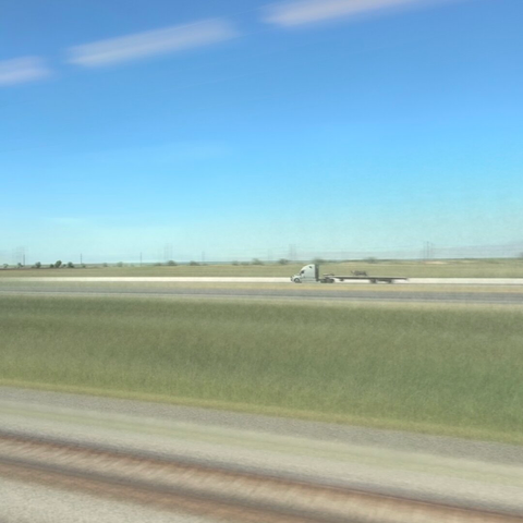 A semi driving down the highway is in focus while everything else is a blur going by.