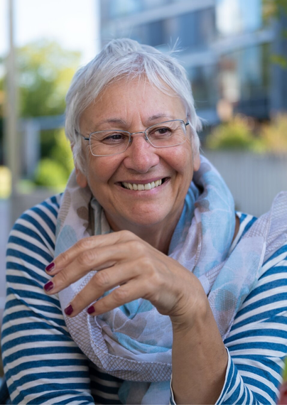 Picture of a smiling old woman. She has short white hair and wears glasses.